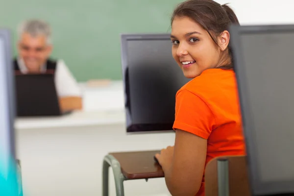 A high school student at a computer, with her instructor working at a computer in the background